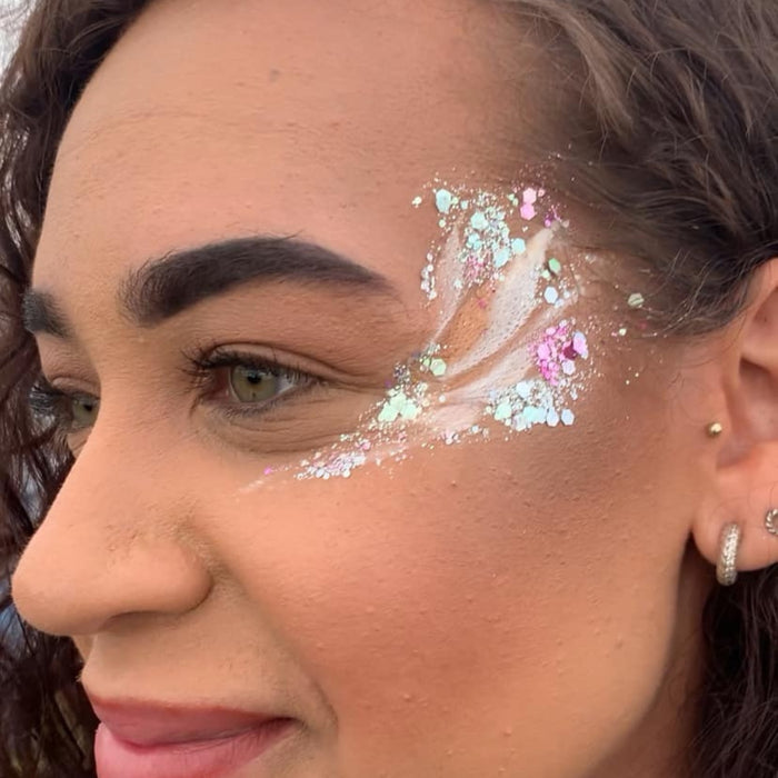 Close-up of a woman's face showing a glitter face paint design on her cheek in pastel pink, mint green, and white.
